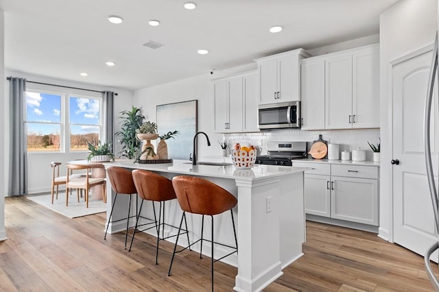 kitchen with stainless steel appliances, white cabinetry, a breakfast bar, and a kitchen island with sink