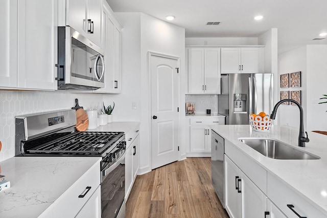 kitchen featuring light hardwood / wood-style floors, appliances with stainless steel finishes, light stone countertops, white cabinets, and sink