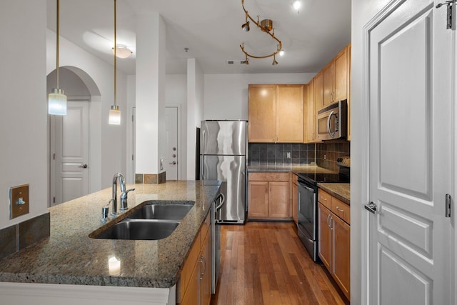 kitchen featuring backsplash, sink, hanging light fixtures, appliances with stainless steel finishes, and dark stone counters