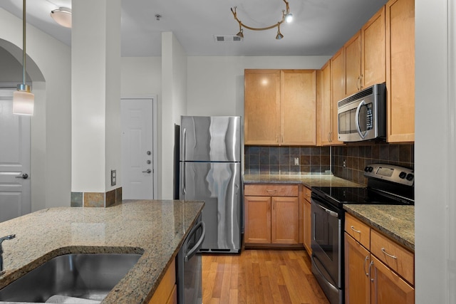 kitchen with backsplash, light hardwood / wood-style floors, pendant lighting, appliances with stainless steel finishes, and dark stone counters