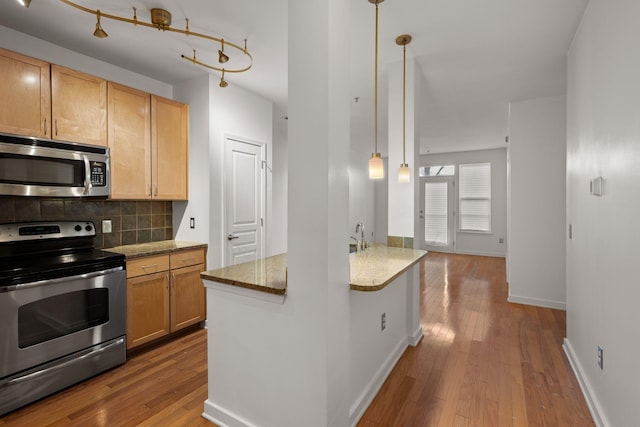 kitchen with hanging light fixtures, light brown cabinetry, light stone counters, and stainless steel appliances