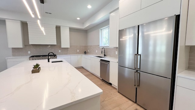 kitchen with light stone counters, stainless steel appliances, a sink, decorative backsplash, and modern cabinets