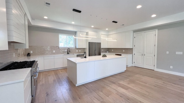 kitchen with stainless steel appliances, visible vents, light countertops, light wood finished floors, and a center island with sink