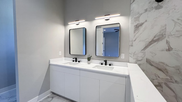 full bath featuring double vanity, marble finish floor, baseboards, and a sink