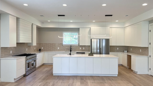 kitchen featuring appliances with stainless steel finishes, light countertops, a center island with sink, and light wood-style flooring