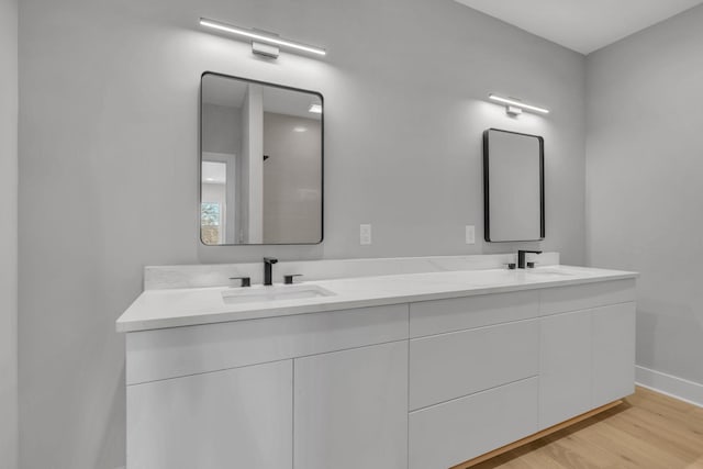 full bathroom with double vanity, wood finished floors, a sink, and baseboards