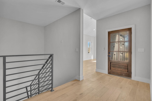 hall with an upstairs landing, wood finished floors, visible vents, and baseboards