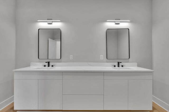 full bath with double vanity, baseboards, and a sink