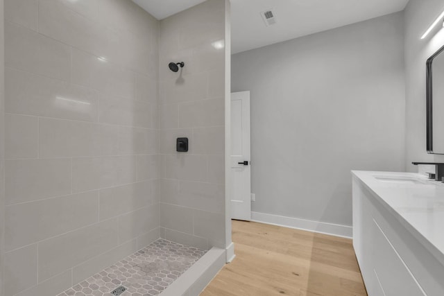 full bath with wood finished floors, vanity, visible vents, baseboards, and tiled shower