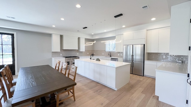 kitchen with appliances with stainless steel finishes, light countertops, a sink, and light wood-style flooring