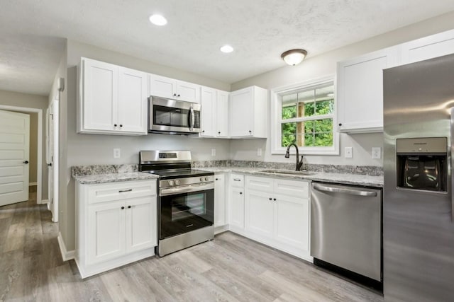 kitchen with light stone countertops, white cabinets, stainless steel appliances, sink, and light hardwood / wood-style flooring