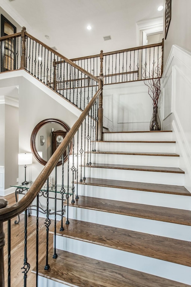 staircase featuring crown molding, wood-type flooring, and a high ceiling