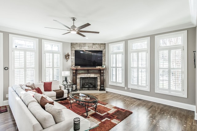 living room with dark hardwood / wood-style floors, ceiling fan, ornamental molding, and a stone fireplace