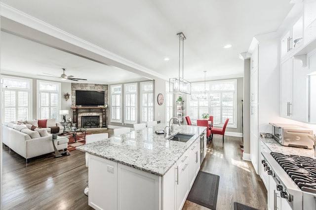 kitchen featuring pendant lighting, white cabinetry, sink, light stone countertops, and a center island with sink