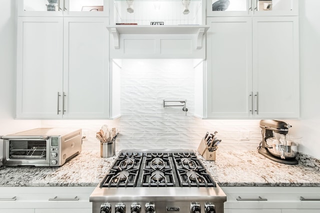 kitchen featuring light stone counters, stove, backsplash, and white cabinets