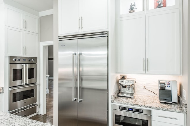 kitchen featuring appliances with stainless steel finishes, dark wood-type flooring, white cabinets, and light stone counters