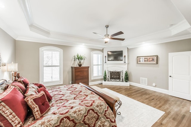 bedroom featuring multiple windows, a tray ceiling, wood-type flooring, and ornamental molding