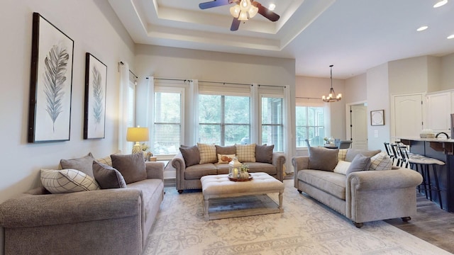 living room with a raised ceiling, ceiling fan with notable chandelier, and light hardwood / wood-style flooring