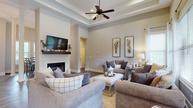 living room with ceiling fan, wood-type flooring, a tray ceiling, and decorative columns