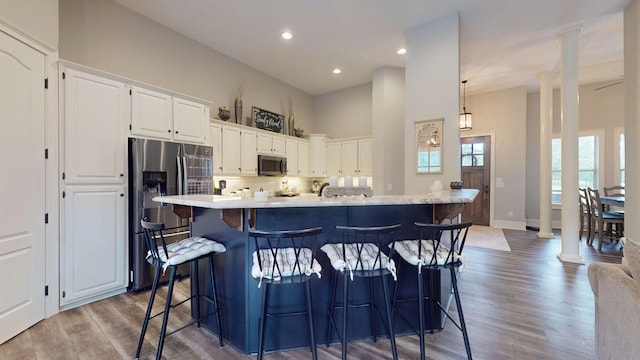 kitchen featuring appliances with stainless steel finishes, white cabinetry, dark hardwood / wood-style flooring, an island with sink, and a breakfast bar