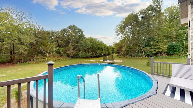 view of pool featuring a wooden deck, a lawn, and a trampoline