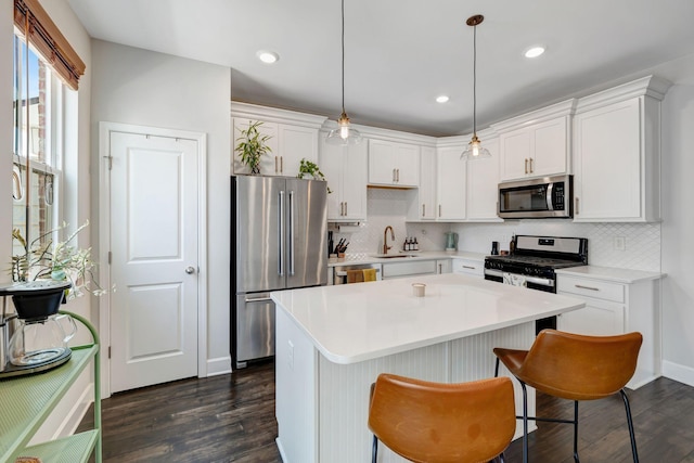 kitchen featuring appliances with stainless steel finishes, dark wood-type flooring, hanging light fixtures, white cabinets, and sink