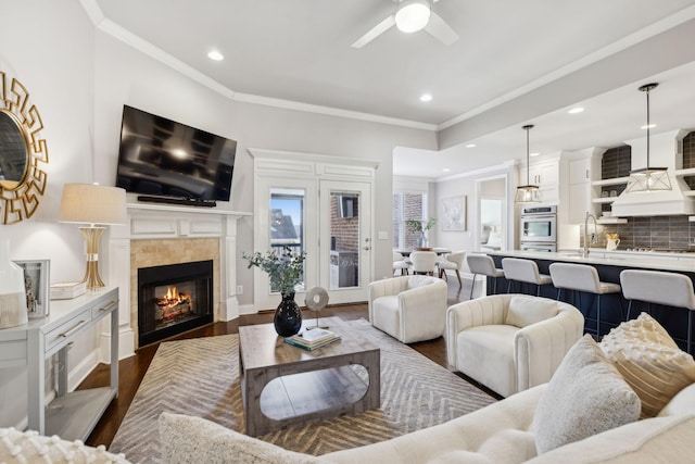 living room featuring sink, dark hardwood / wood-style floors, ornamental molding, ceiling fan, and a tile fireplace