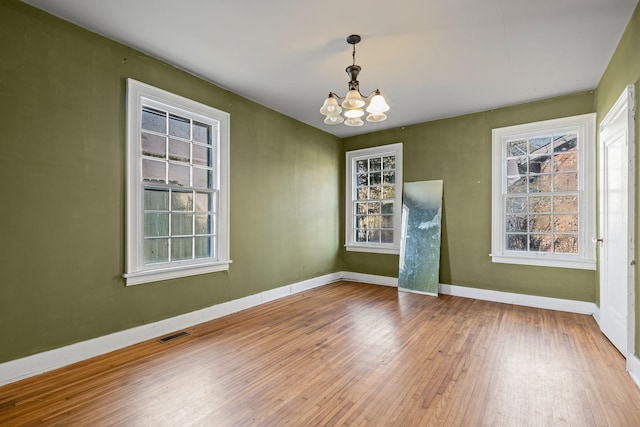 empty room featuring wood-type flooring and a notable chandelier