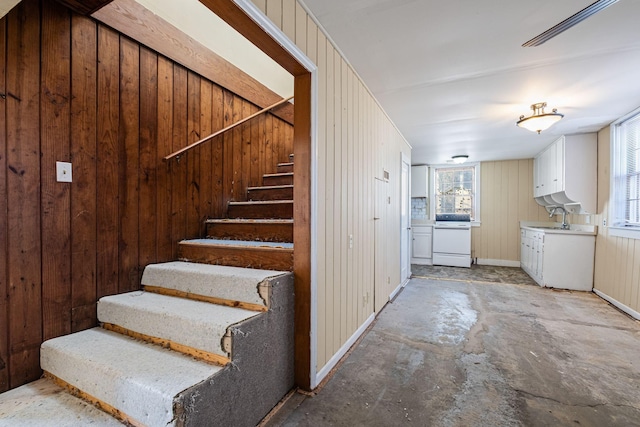 staircase featuring sink, wooden walls, and concrete floors