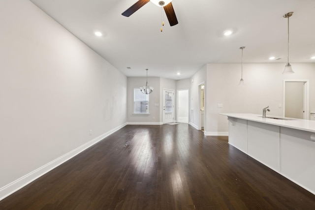 unfurnished living room with dark hardwood / wood-style floors, sink, and ceiling fan with notable chandelier