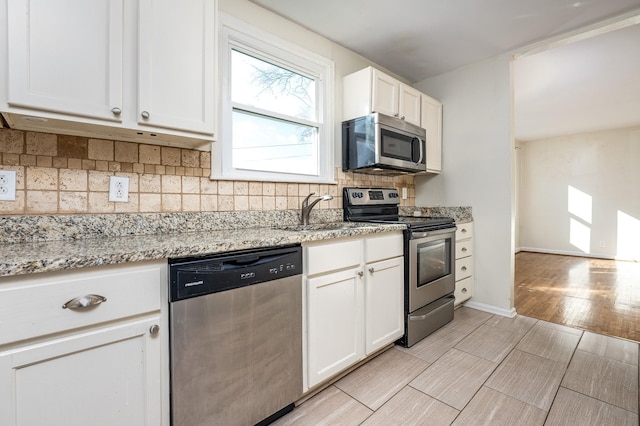 kitchen featuring stainless steel appliances, white cabinetry, light stone counters, and sink