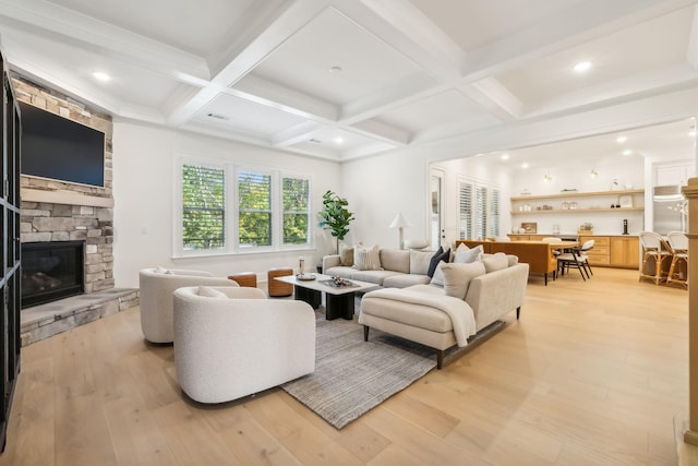 living room with coffered ceiling, a stone fireplace, beamed ceiling, and light wood-type flooring