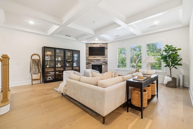 living room with beam ceiling, a stone fireplace, and light wood-type flooring