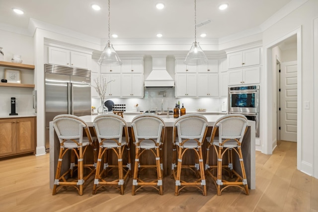 kitchen with hanging light fixtures, stainless steel appliances, custom range hood, and white cabinets