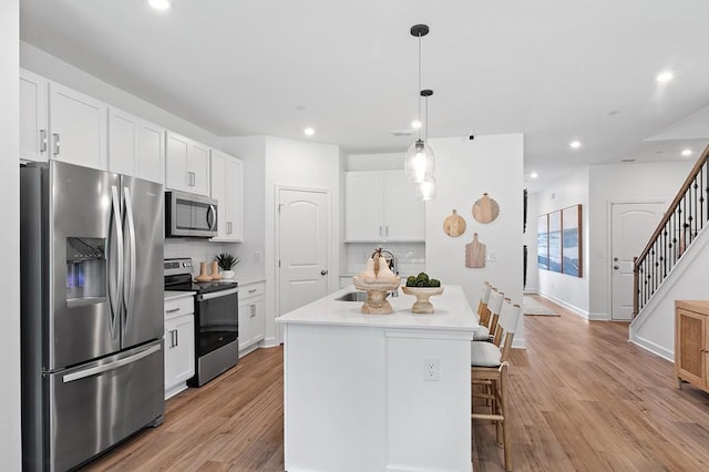 kitchen featuring stainless steel appliances, backsplash, decorative light fixtures, white cabinets, and a center island