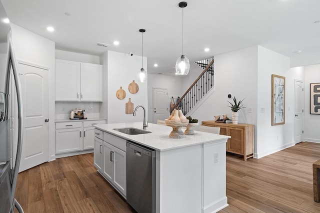 kitchen featuring a center island with sink, sink, white cabinetry, hanging light fixtures, and appliances with stainless steel finishes