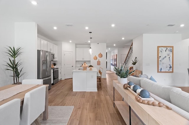 kitchen featuring a kitchen island, pendant lighting, light hardwood / wood-style flooring, stainless steel appliances, and white cabinets