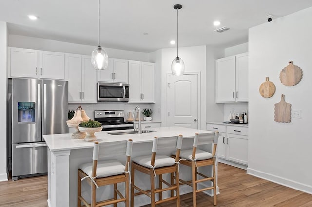 kitchen featuring appliances with stainless steel finishes, decorative backsplash, white cabinetry, and an island with sink