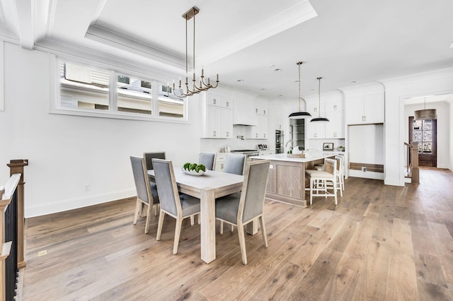 dining area featuring a raised ceiling, light wood-type flooring, sink, and ornamental molding