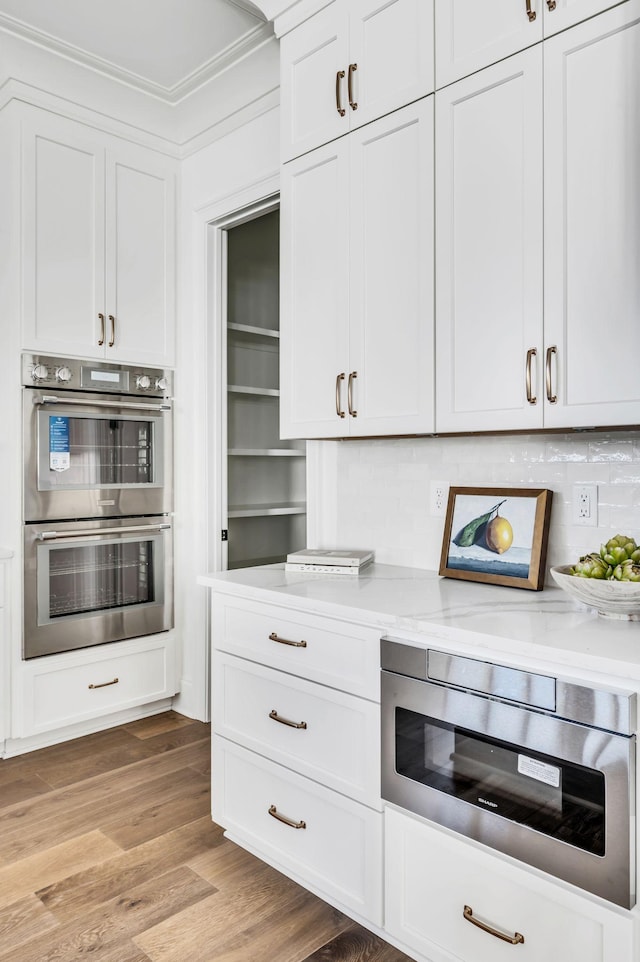 kitchen featuring white cabinetry, double oven, decorative backsplash, light wood-type flooring, and light stone counters