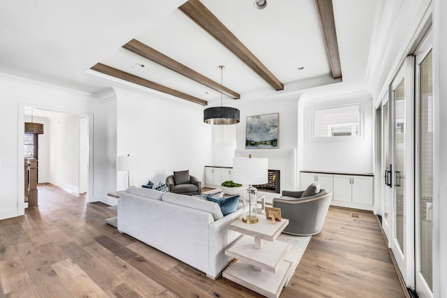 living room featuring a brick fireplace, beamed ceiling, crown molding, and light hardwood / wood-style flooring