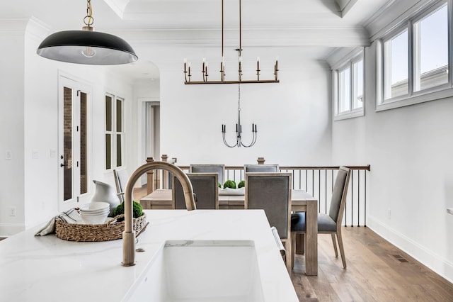 dining space featuring sink, light wood-type flooring, ornamental molding, and an inviting chandelier