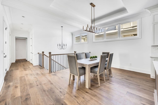 dining space with a tray ceiling, light hardwood / wood-style flooring, ornamental molding, and an inviting chandelier