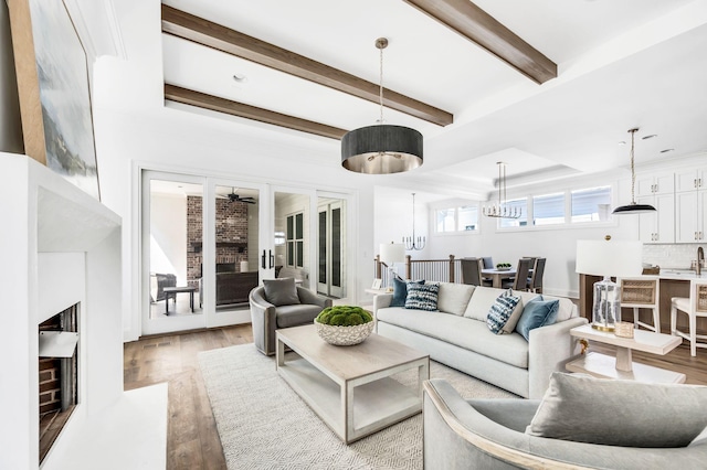 living room featuring beam ceiling, a tray ceiling, ceiling fan with notable chandelier, and light hardwood / wood-style flooring