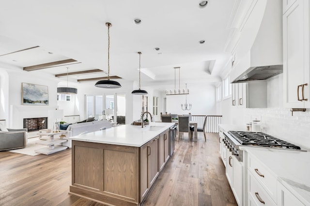 kitchen featuring custom exhaust hood, white cabinetry, stainless steel appliances, hanging light fixtures, and a kitchen island with sink