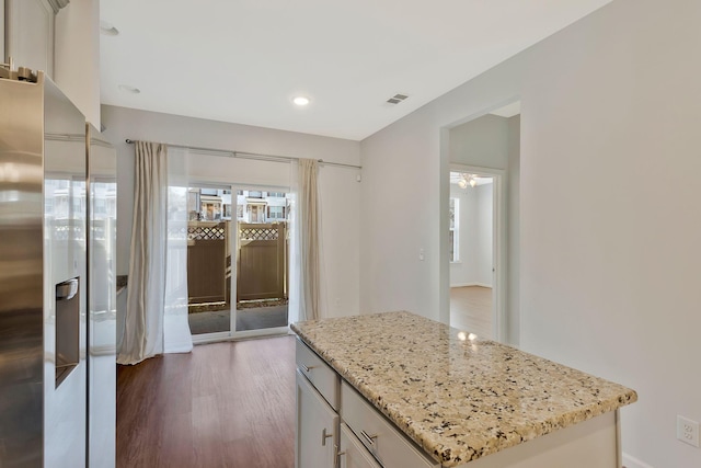 kitchen with white cabinets, a kitchen island, refrigerator with ice dispenser, light stone counters, and dark hardwood / wood-style floors