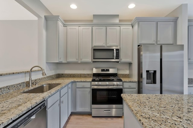 kitchen with sink, light wood-type flooring, light stone countertops, and appliances with stainless steel finishes