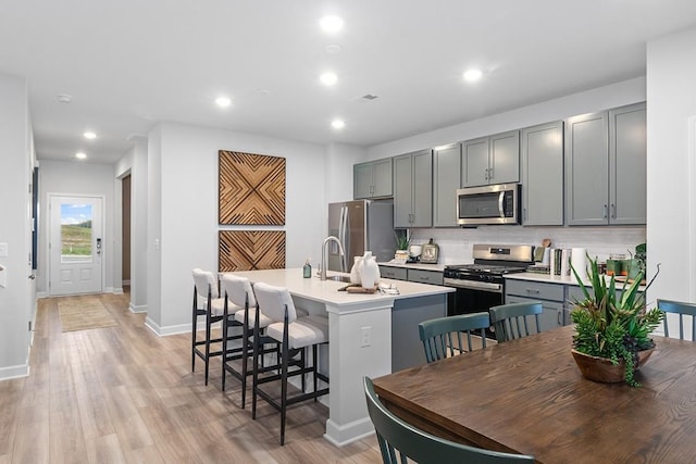 kitchen with a center island with sink, appliances with stainless steel finishes, gray cabinetry, backsplash, and a kitchen breakfast bar