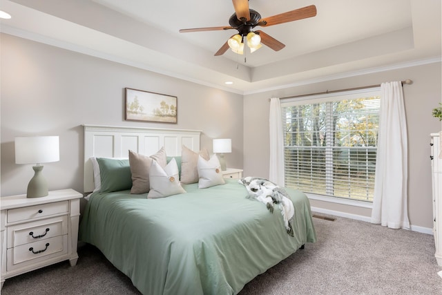 carpeted bedroom featuring ceiling fan, multiple windows, and a tray ceiling