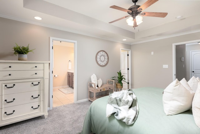 bedroom with ceiling fan, connected bathroom, a tray ceiling, light colored carpet, and ornamental molding